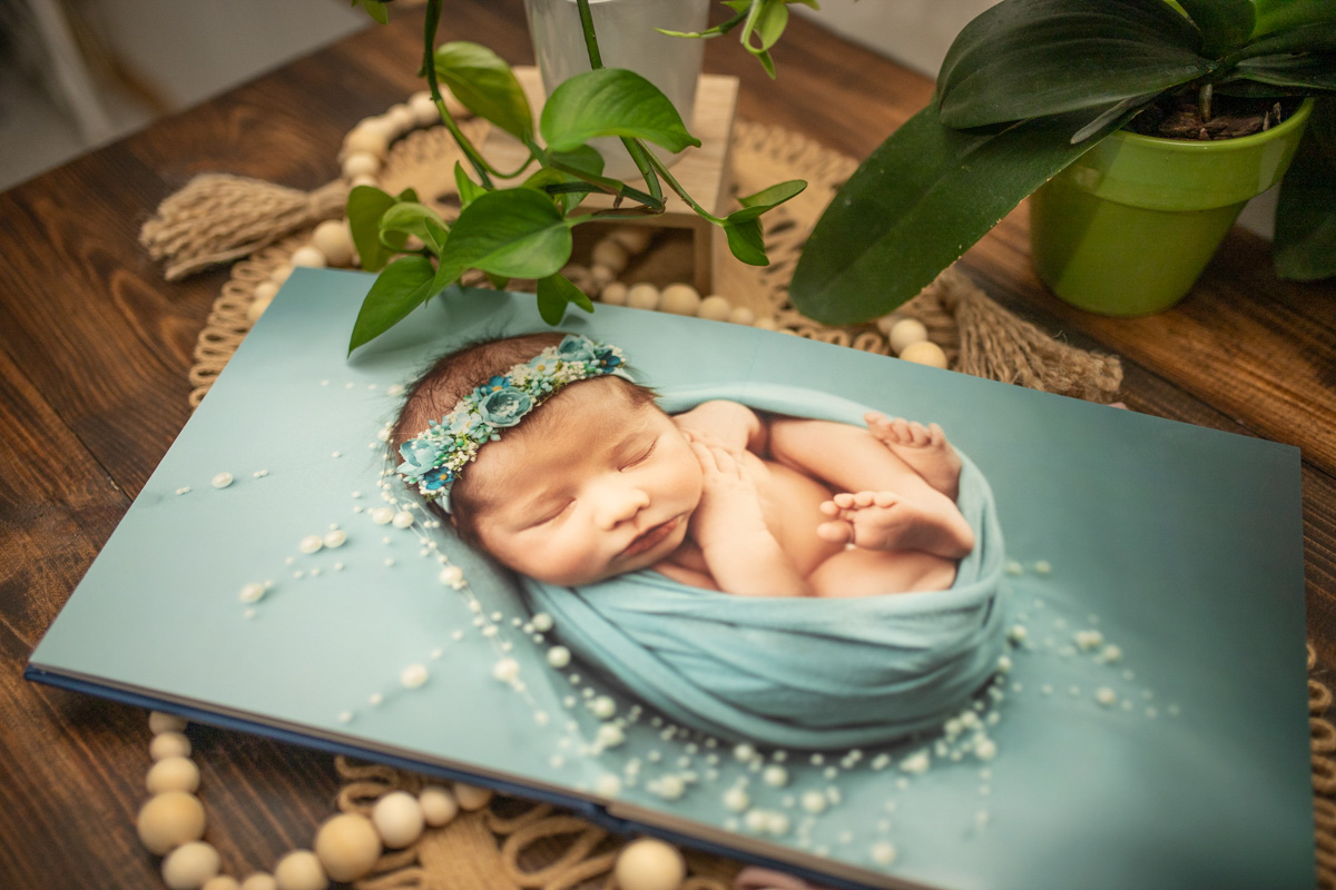 fine art album of newborn photography session on wood floor with greenery and beaded hanging minneapolis newborn photographer