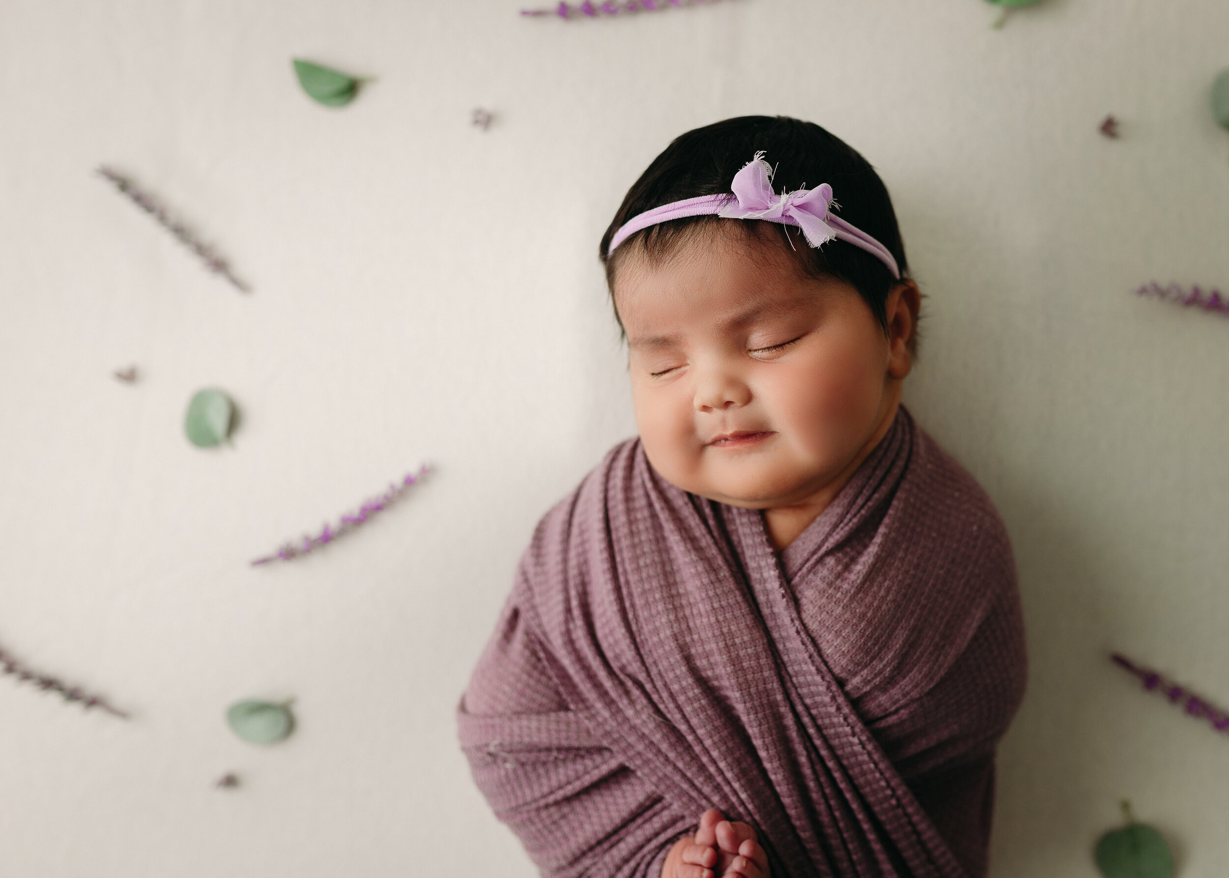 baby girl in lavendar on cream backdrop with lavender branches and leaves for kona Hawaii big island newborn photographer session