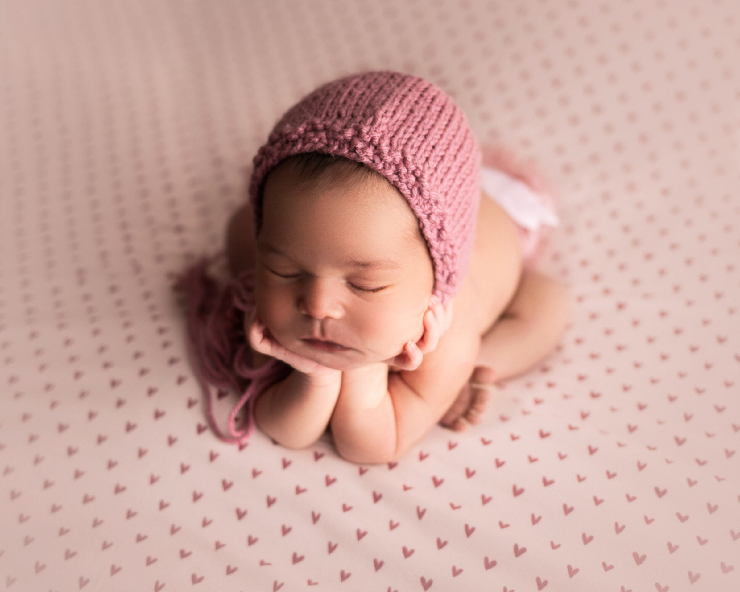 newborn girl on heart backdrop in froggy pose with pink bonnet by baby photographer in Kona mn