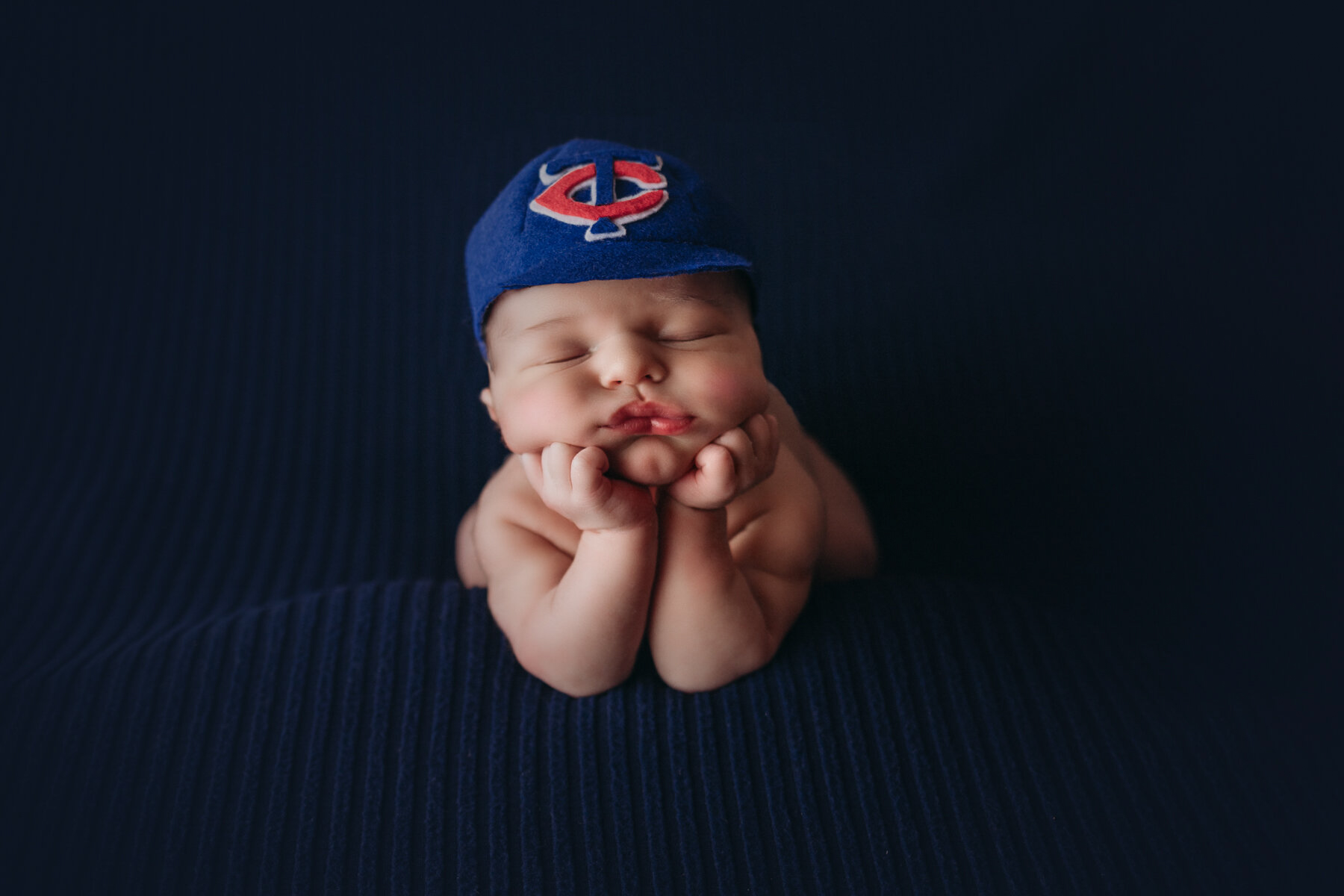baby boy in froggy pose on navy blue with twins baseball hat for newborn session in minneapolis st paul mn
